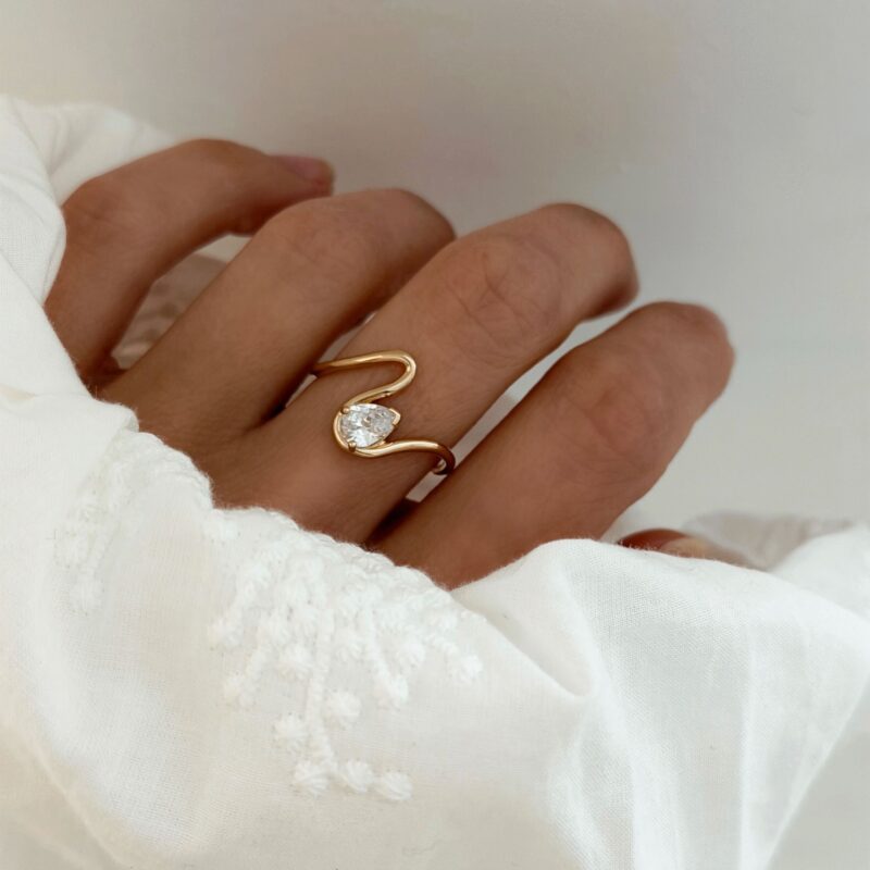 Bague pour femme en plaqué or 3 microns 18 carats à la forme originale. Le bijou se compose d'un design à la forme de vague, monté d'un oxyde de zirconium en forme de goutte.