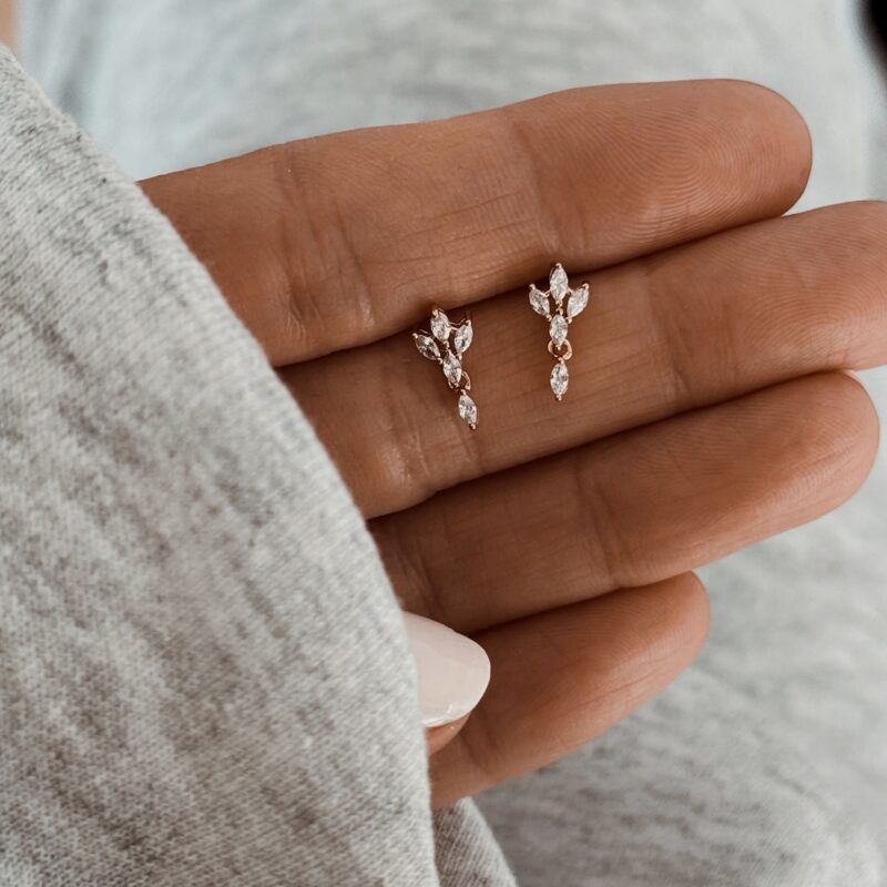 Boucles d'oreilles pour femme en plaqué or 3 microns 18 carats qui résistent à l'eau. Ces boucles sont discrètes, raffinées et très agréables à porter. Elles se composent de 5 petits oxydes de zirconium. Les 4 premiers forment une fleur et le dernier vient souligner le motif floral, juste en dessous, comme petit pendant. Le bijou mesure 0,5 centimètres sur 1,2 centimètres. La paire de boucles se ferment à l'aide d'un fermoir papillon. Tous nos bijoux sont garanties sans nickel, sans cadmium, sans sel de plomb.