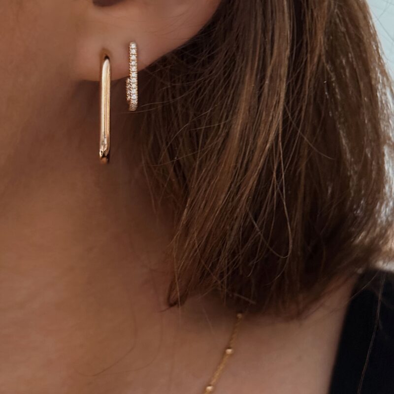 Association de boucles d'oreilles pendantes en plaqué or 3 microns 18 carats. La première est une créole en forme de rectangle et la seconde se compose d'une barre pendante, recourbée à l'extrémité vers le haut. Cette paire est entièrement recouverte de petits oxydes de zirconium sur le dessus.