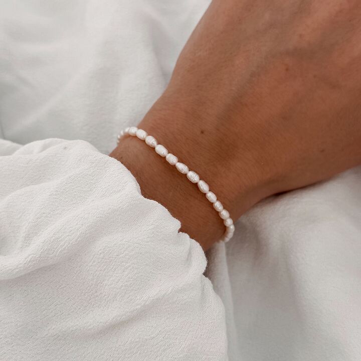 Bracelet raffiné pour femme décoré de petites perles d'eau douce blanches à la forme allongées. Finition du bracelet en acier inoxydable doré. Longueur du bracelet : 21 centimètres Fermoir mousqueton sécurisé.