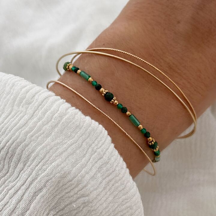Association bracelets plaqué or et d'un bracelet décoré de perles vertes.