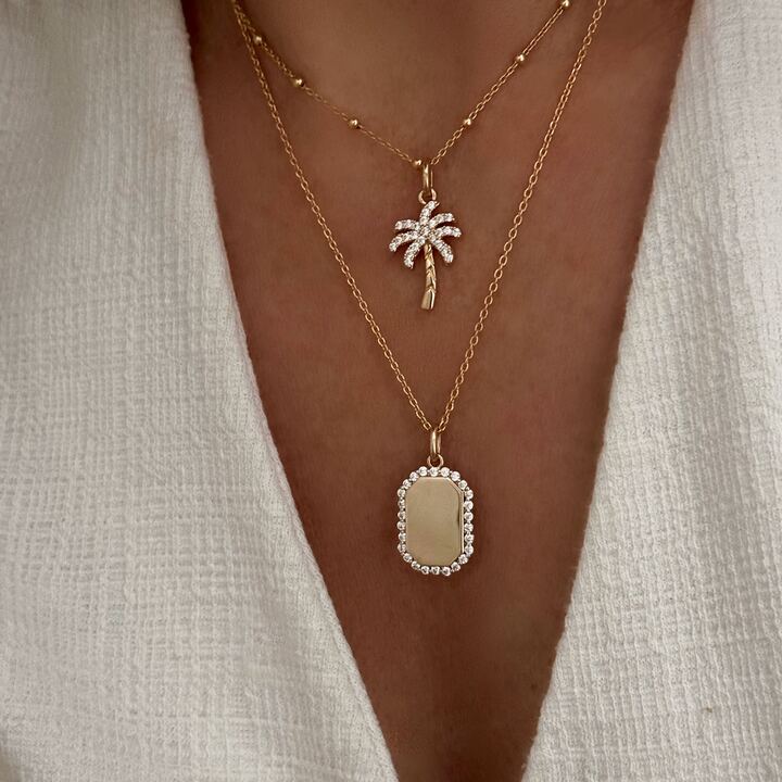 Association de colliers en plaqué or pour femme. Le premier collier est décoré d'un pendentif en forme de palmier. Le second se compose d'un pendentif personnalisable avec une gravure, de forme rectangulaire.