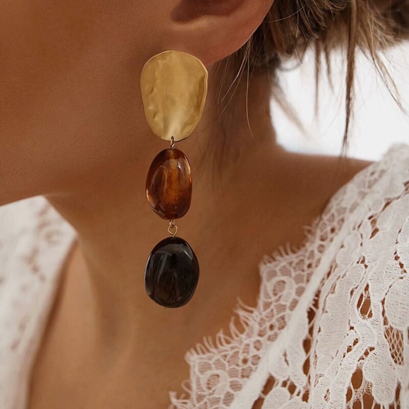 Boucles d'oreilles pour femme pendantes en acier inoxydable doré. La paire se compose d'une première pièce à la forme organise de couleur doré au fini brossé et de deux perles marrons xxl.
