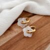Boucles d'oreilles type créoles en acier inoxydable doré décoré de petites fleurs en acétate blanc. La paire de boucles Flory est disponible avec des fleurs de différentes couleurs : vert, rose, beige, marron, noir, jaune etc...