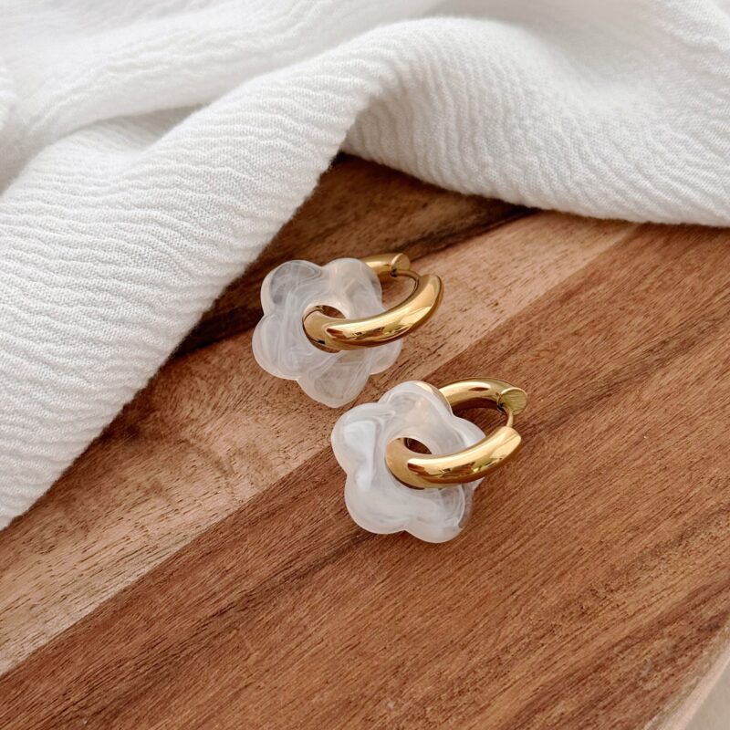 Boucles d'oreilles type créoles en acier inoxydable doré décoré de petites fleurs en acétate blanc. La paire de boucles Flory est disponible avec des fleurs de différentes couleurs : vert, rose, beige, marron, noir, jaune etc...
