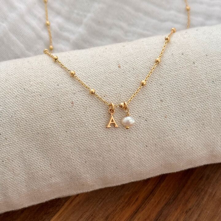 Collier personnalisable en plaqué or 3 microns 18 carats pour femme. Le bijou se compose d'une fine chaîne décorée de petites boules et d'un pendentif en forme de lettre et d'une perle d'eau douce. La lettre mesure 0,7 cm. À vous de personnaliser votre collier avec la lettre de votre choix via notre formulaire de personnalisation.