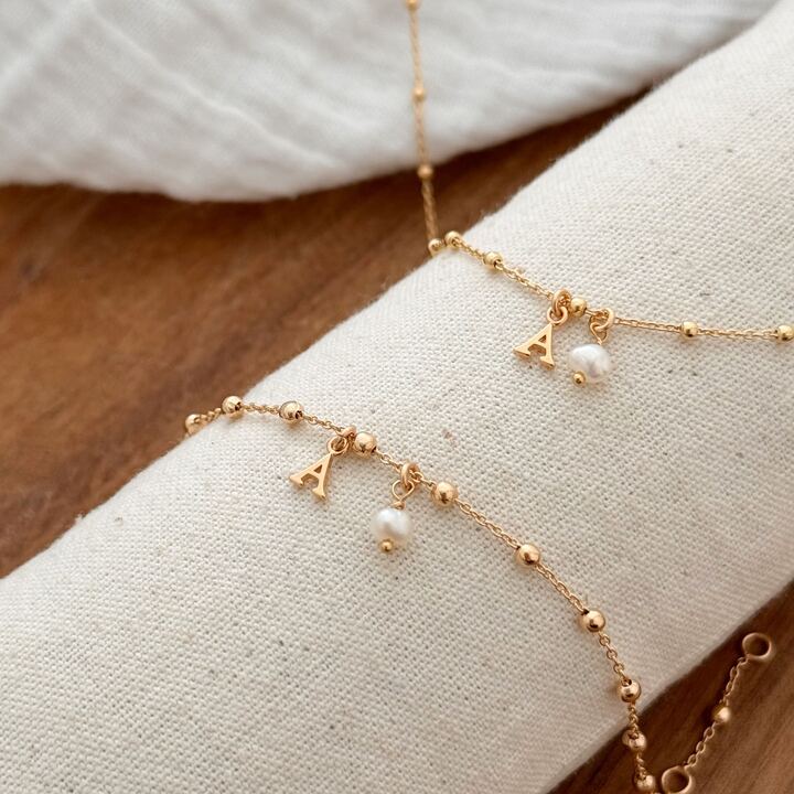 Parure de bijoux pour femme en plaqué or 3 microns 18 carats qui se compose d'un bracelet et d'un collier, tous les deux réalisé à partir d'une fine chaîne décorée de petites billes. Le collier et le bracelet sont personnalisable avec la lettre de votre choix. Une petite perle d'eau douce vient se placé à côté de la lettre pour apporter une touche de douceur.