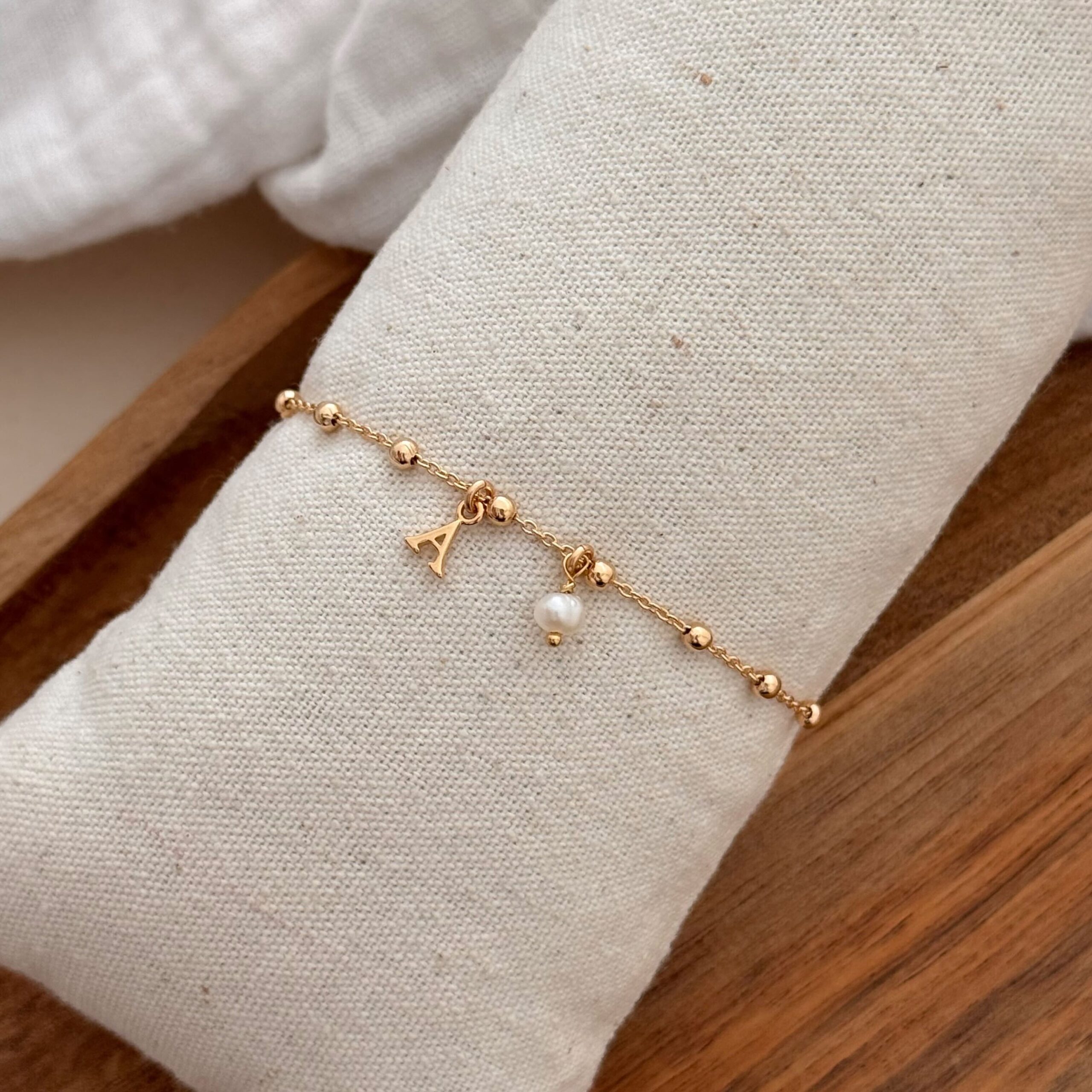 Bracelet pour femme en plaqué or 3 microns 18 carats qui se compose d'une fine chaîne décorée de petites boucles. La chaîne est ornée d'un pendentif en forme de lettre et d'une petite perle d'eau douce. Choisissez de personnaliser votre bracelet avec la lettre de votre choix parmi les 26 lettres de l'alphabet.