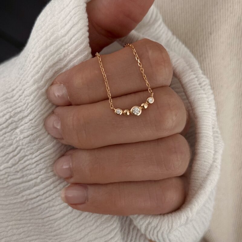 Collier en plaqué or 3 microns 18 carats Le bijou se compose d'une barrette sertie de 3 oxydes de zirconium et de deux billes dorées Longueur : 1.5 cm Ajustable à 40, 42 et 45 cm Fermoir mousqueton ovale