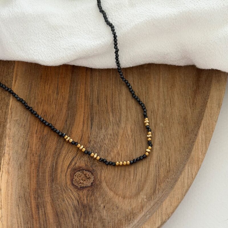 Collier pour femme en acier inoxydable doré décoré de petites perles noires et dorés. Un adorable collier ras-de-cou qui se porte avec tout type de tenue. Taille ajustable de 38 à 43 centimètres. Fermoir mousqueton ovale.