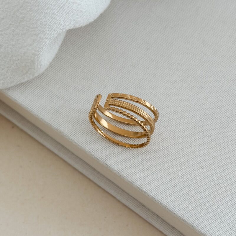 Bague large en acier inoxydable doré Le bijou se compose de 3 anneaux de différents styles  Largeur : 0.9 cm Taille légèrement ajustable du 54 à 56 Cette bague est garantie sans nickel, sans cadmium, sans sel de plomb Elle résiste à l’eau et ne noircit pas