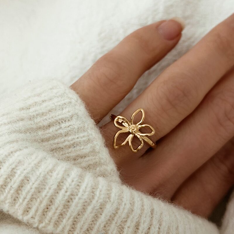 Bague pour femme en acier inoxydable doré à la taille ajustable. Le bijou est monté d'un motif floral composé de pétales à la forme irrégulière.