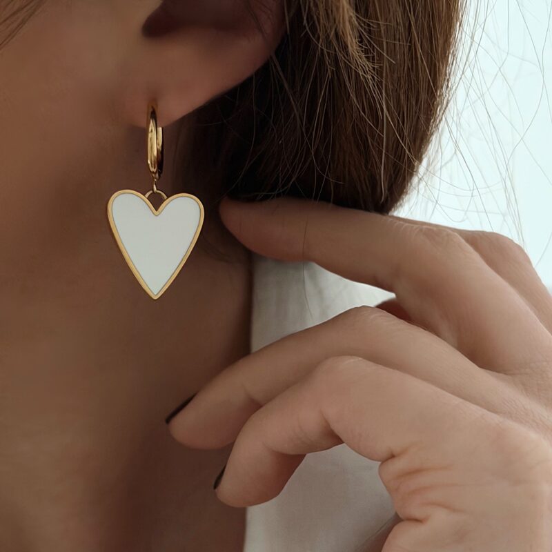 Boucles d'oreilles type créoles pendantes en acier inoxydable doré Le bijou se compose d'une fine créole et d'un pendentif en forme de cœur, émaillé en blanc Diamètre créole : 1,5 cm Dimensions cœur : 1,7 x 2 cm Longueur boucle d'oreille : 3,6 cm Fermoir charnière Cette paire de boucles d'oreilles est garantie sans nickel, sans cadmium, sans sel de plomb. Elle résiste à l’eau et ne noircit pas
