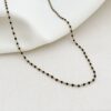 Collier pour femme tendance fin et minimaliste en acier inoxydable doré. Le collier est décoré de petites billes émaillées en noir. Taille tour de cou ajustable.