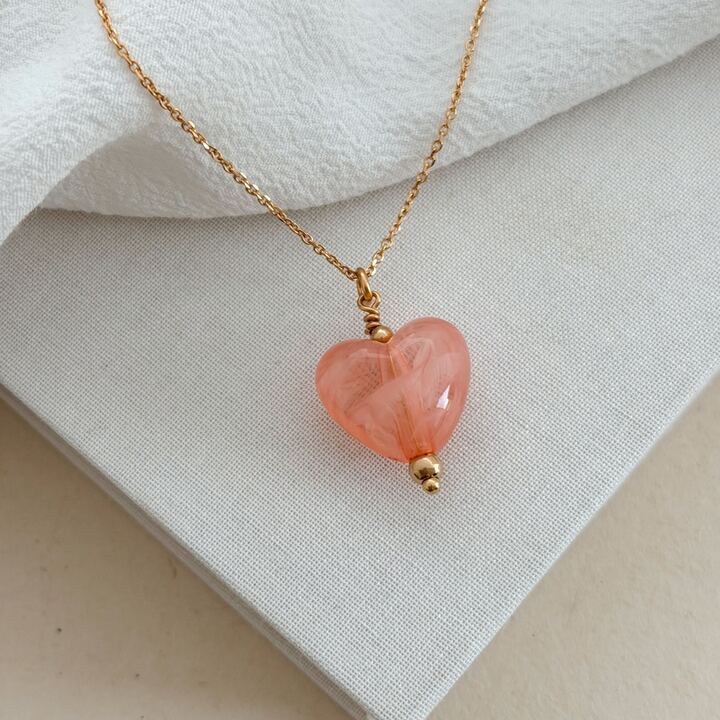 Collier en plaqué or 3 microns 18 carats décoré d'un pendentif en forme de coeur bombé en acrylique rose, marron ou beige. Le collier se porte en sautoir et est disponible en 60,70 ou 80 centimètres.