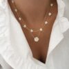 Association de colliers fins tendance pour femme en acier inoxydable doré. Le premier collier est décoré de petits coeur en nacre et le seconde est orné d'un pendentif en forme de fleur également en nacre.