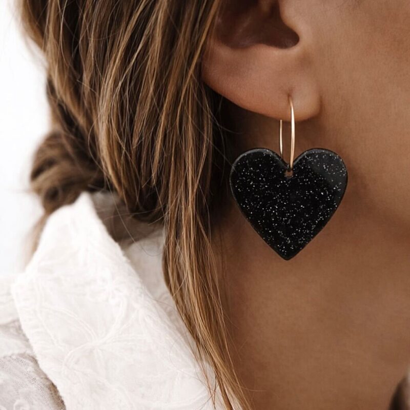 Boucles d'oreilles pendantes en plaqué or 3 microns 18 carats qui se compose d'une créole et d'un grand coeur noir en acrylique, avec un fini pailleté.