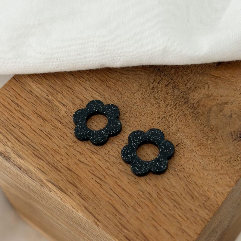 Boucles d'oreilles interchangeables pour femme, le must-have bijoux du moment ! Découvrez notre paire de fleurs en acétate, coloris noir effet pailleté. Ce bijou sera à glisser sur votre paire de boucles d'oreilles type créoles favorite ! Diamètre de la fleur : 0,8 centimètres.