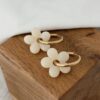 Boucles d'oreille pour femme tendance qui se compose d'une grande paire de créoles dorée fines, décorées d'une jolie fleur beige au relief légèrement bombé.