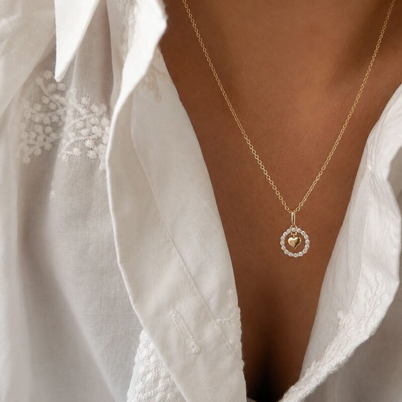 Collier pour femme en plaqué or 3 microns 18 carats qui se compose d'une chaîne fine, classique, décorée d'un petit pendentif rond ajouré, sertie de petits oxydes de zirconium et décoré d'un coeur en son centre.